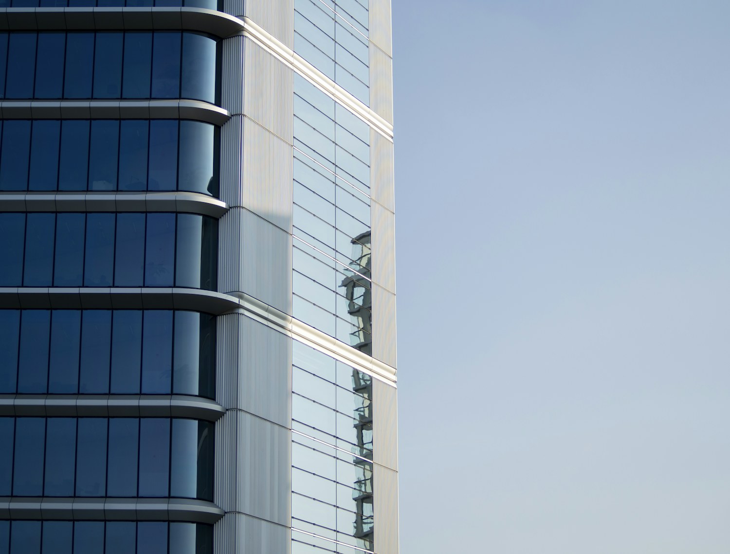 The curved glass and steel corner of a modern office tower against a clear sky