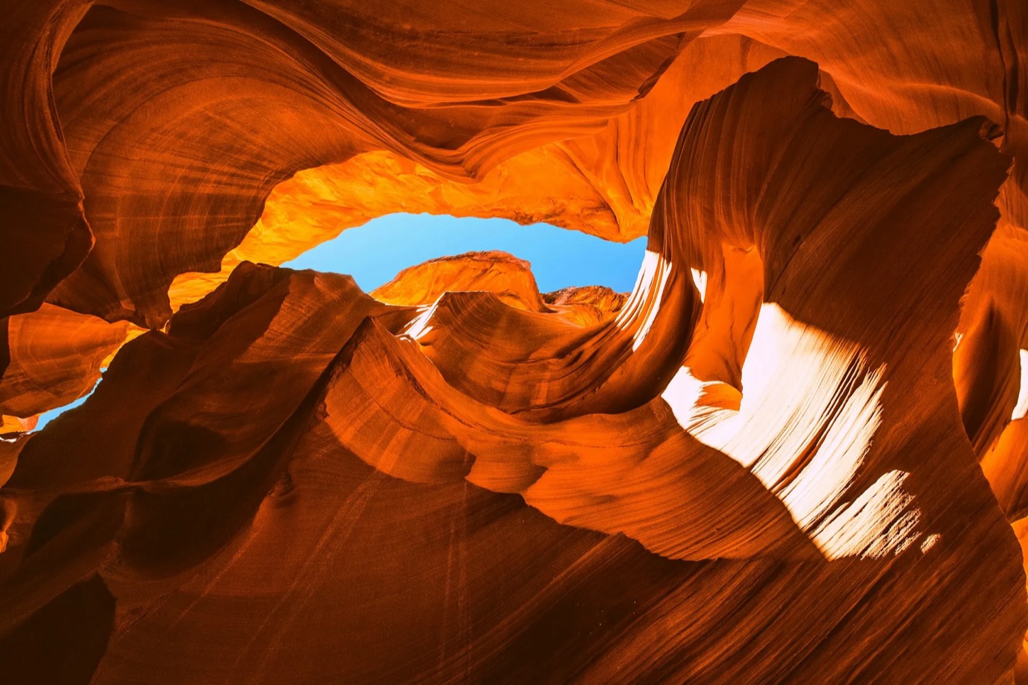 A sunlit sandstone slot canyon opening onto a bright blue sky