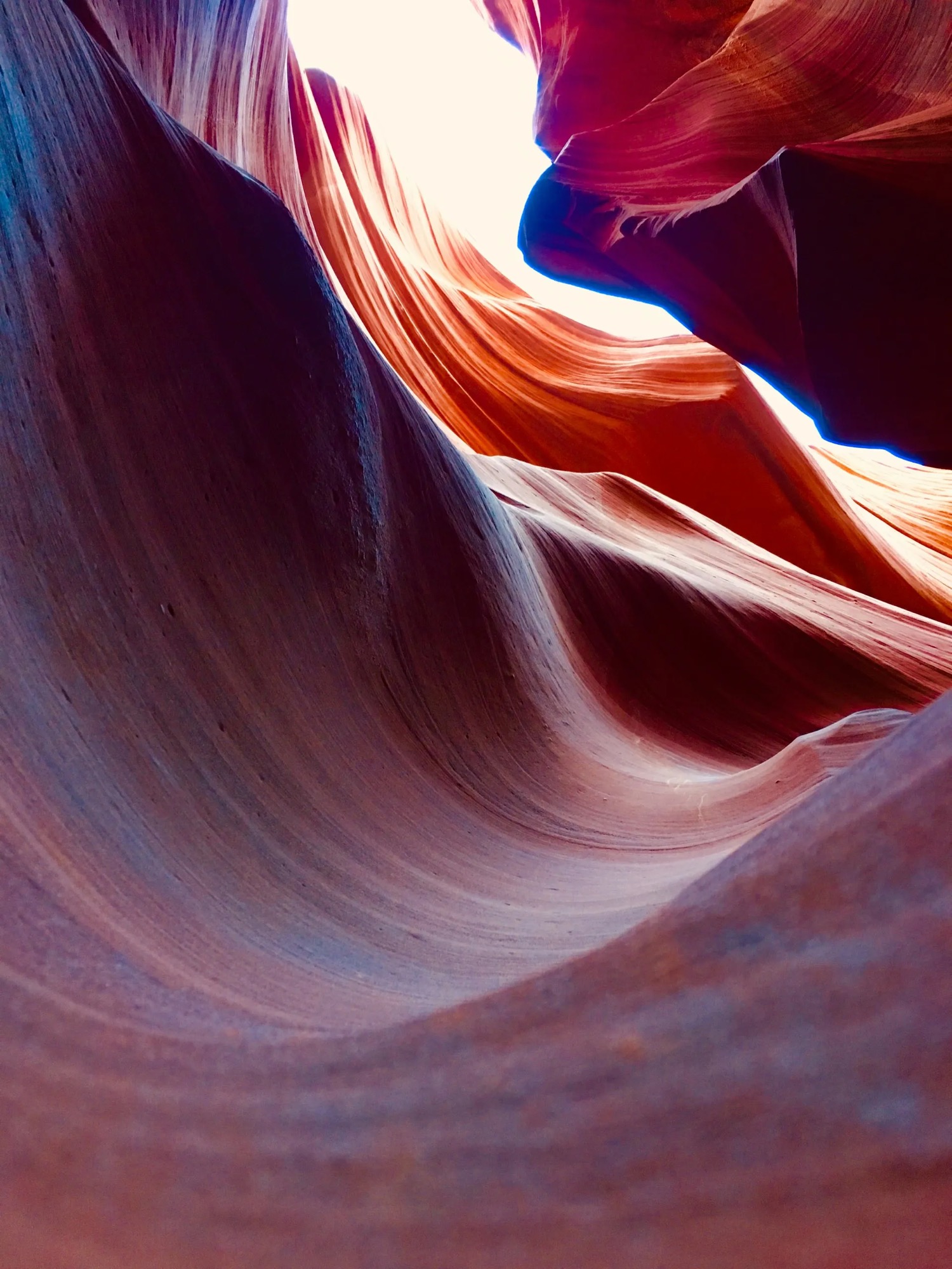 Deep red and blue-lit sandstone canyon walls opening onto bright sky