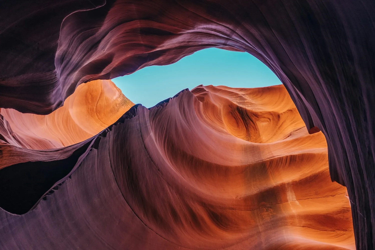 A dramatic sandstone slot canyon opening onto blue sky, walls in deep purple and orange